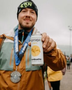 Závodník Spartan Race Lipno 2025 drží kombuchu Spraga Original po doběhnutí závodu